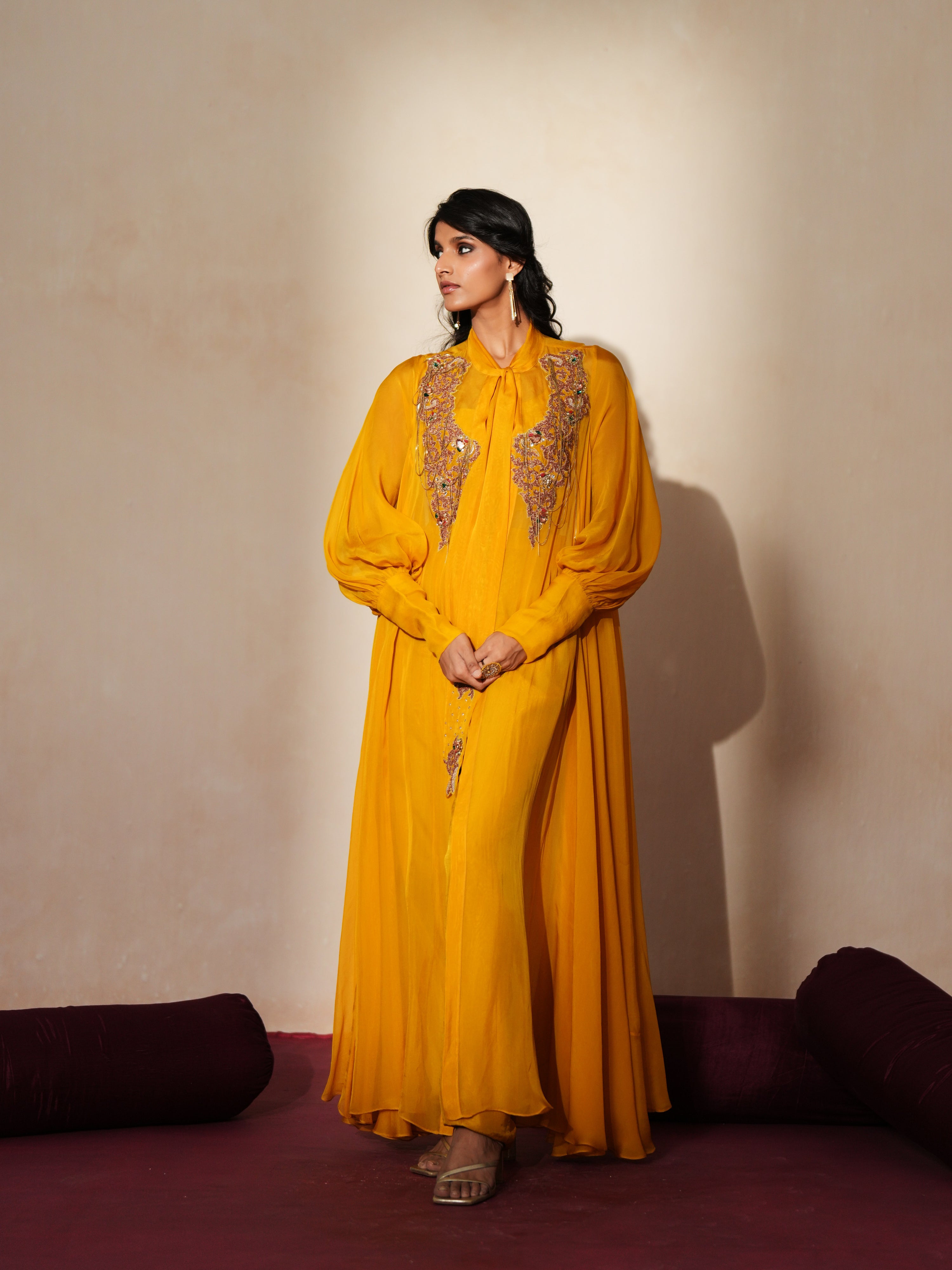 Woman in a golden yellow traditional outfit standing againsta beige wall on a red carpet.