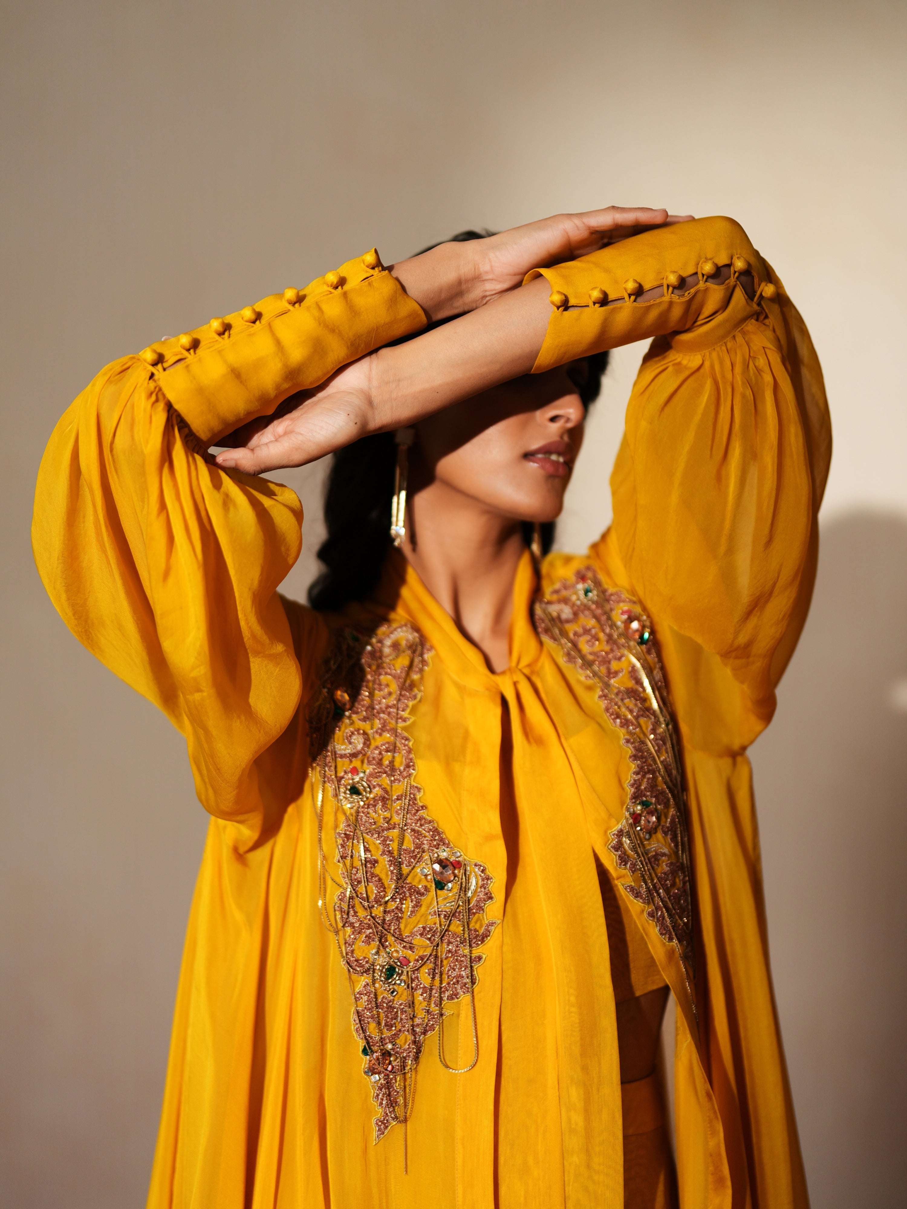Woman in a golden yellow traditional outfit standing againsta beige wall on a red carpet.