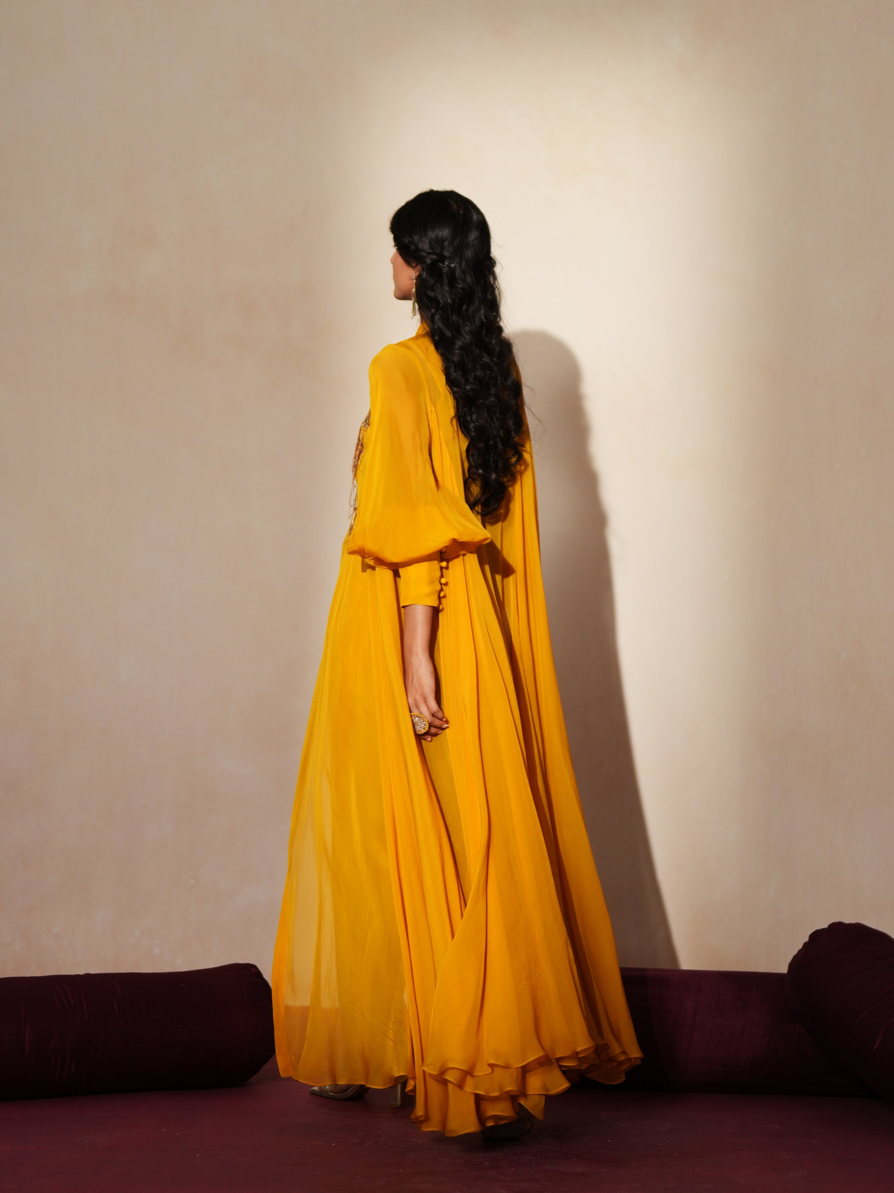 Woman in a golden yellow traditional outfit standing againsta beige wall on a red carpet.