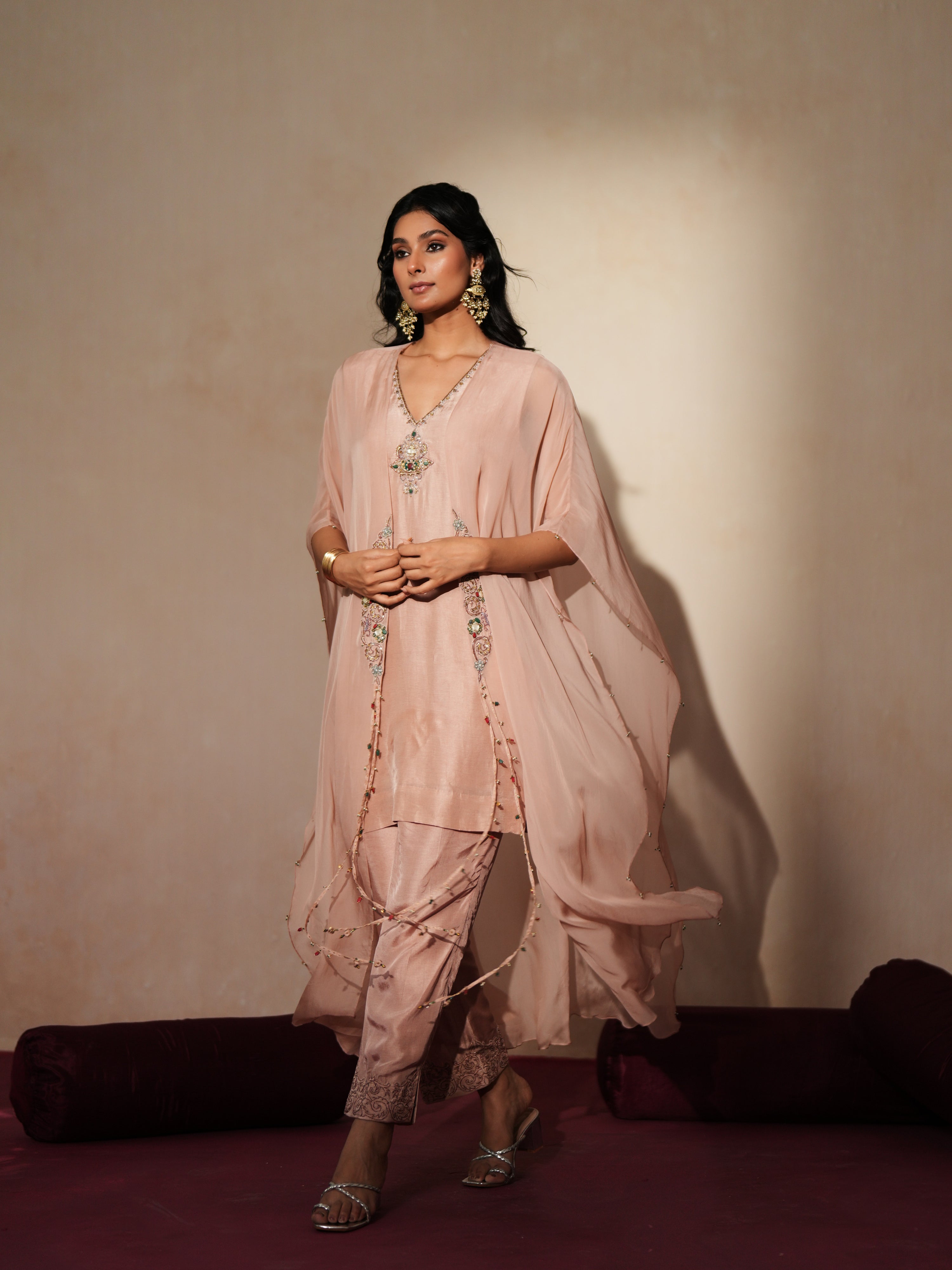 Woman in a soft pink traditional outfit standing againsta beige wall on a red carpet.