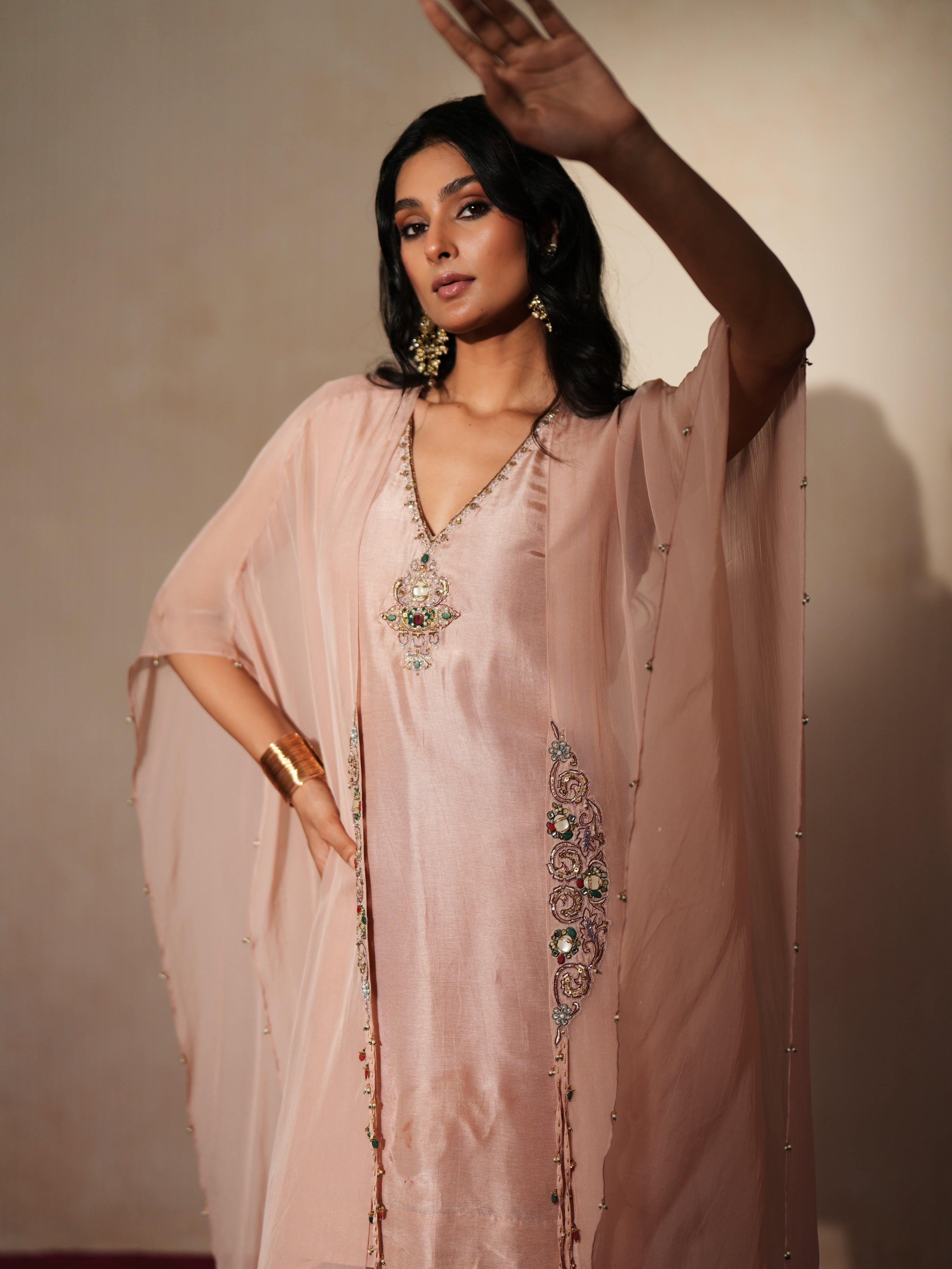 Woman in a soft pink traditional outfit standing againsta beige wall on a red carpet.
