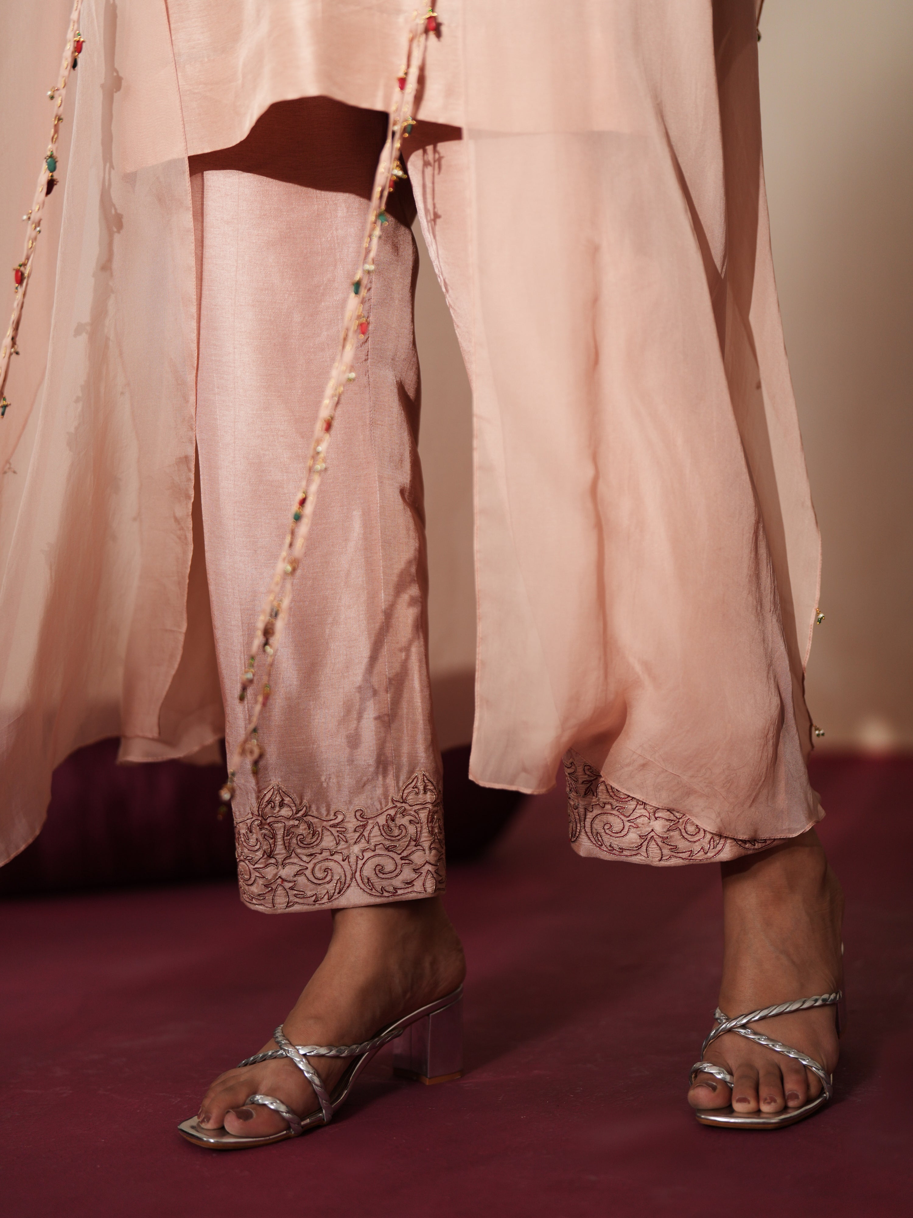 Woman in a soft pink traditional outfit standing againsta beige wall on a red carpet.