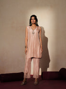 Woman in a soft pink traditional outfit standing againsta beige wall on a red carpet.