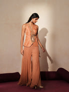 Woman in a metallic mocha  traditional outfit standing againsta beige wall on a red carpet.