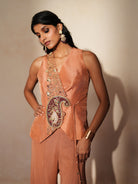 Woman in a metallic mocha  traditional outfit standing againsta beige wall on a red carpet.