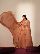 Woman in a metallic mocha  traditional outfit standing againsta beige wall on a red carpet.