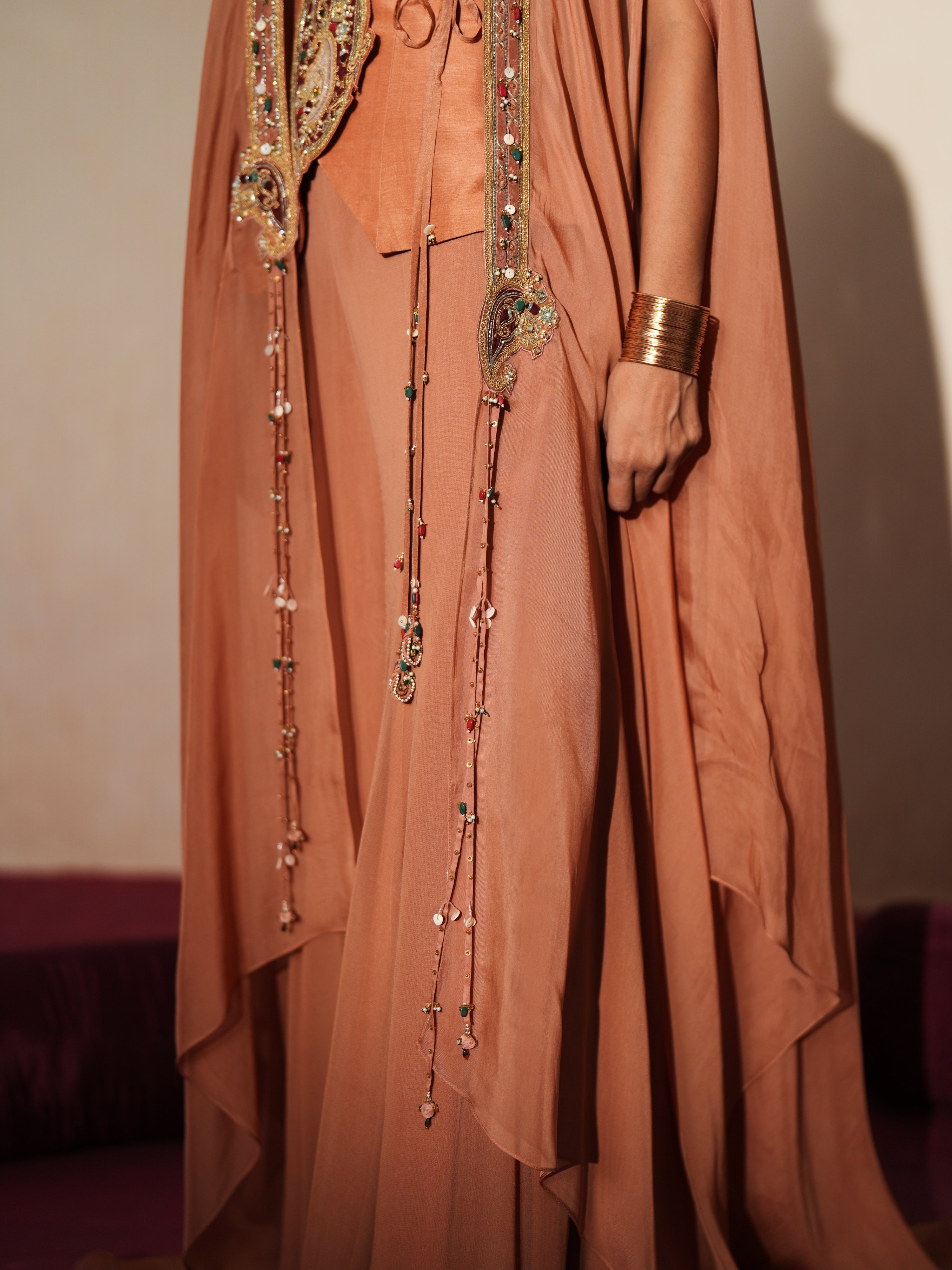 Woman in a metallic mocha  traditional outfit standing againsta beige wall on a red carpet.