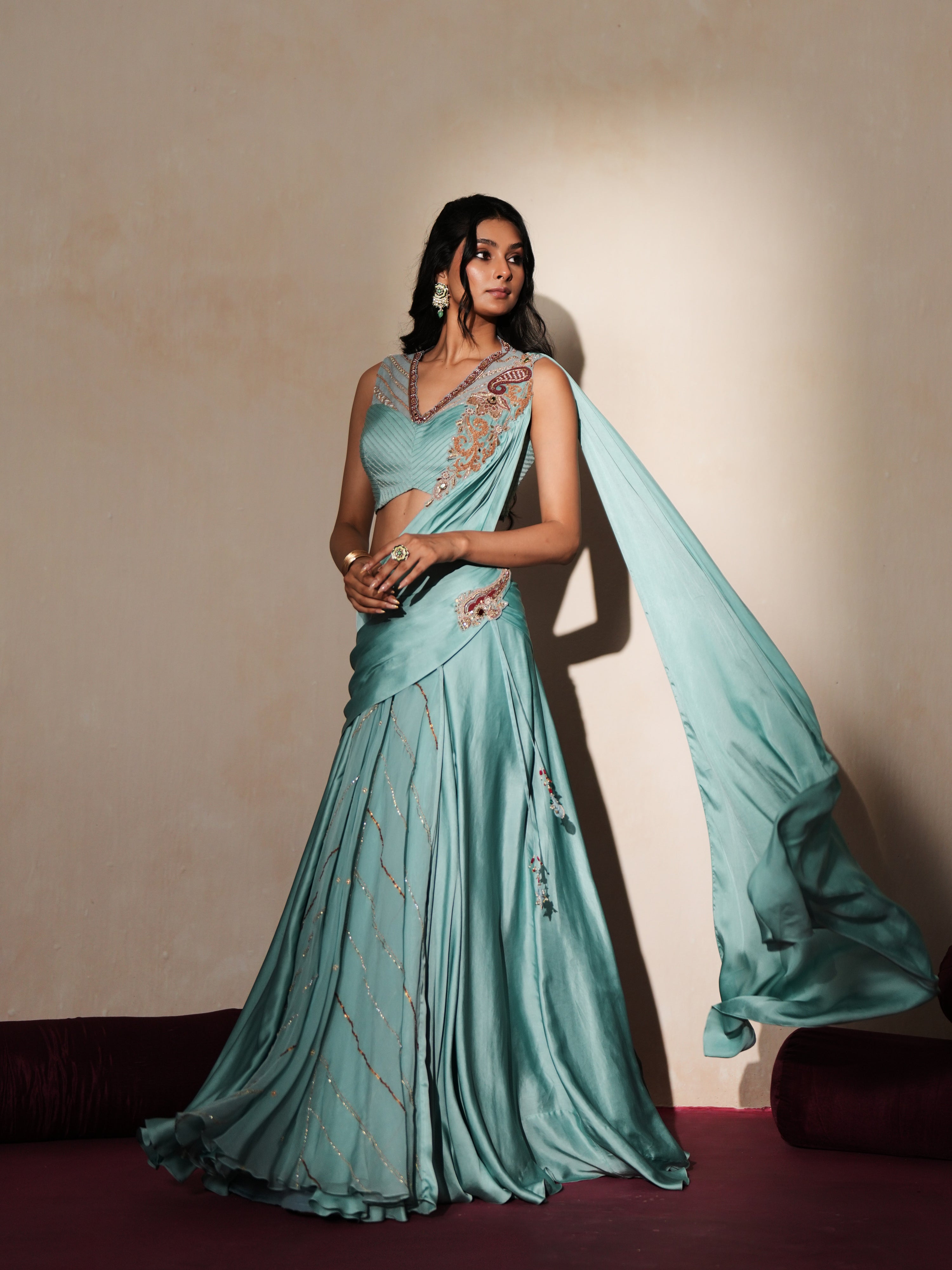 Woman in a pastel blue traditional outfit standing againsta beige wall on a red carpet.