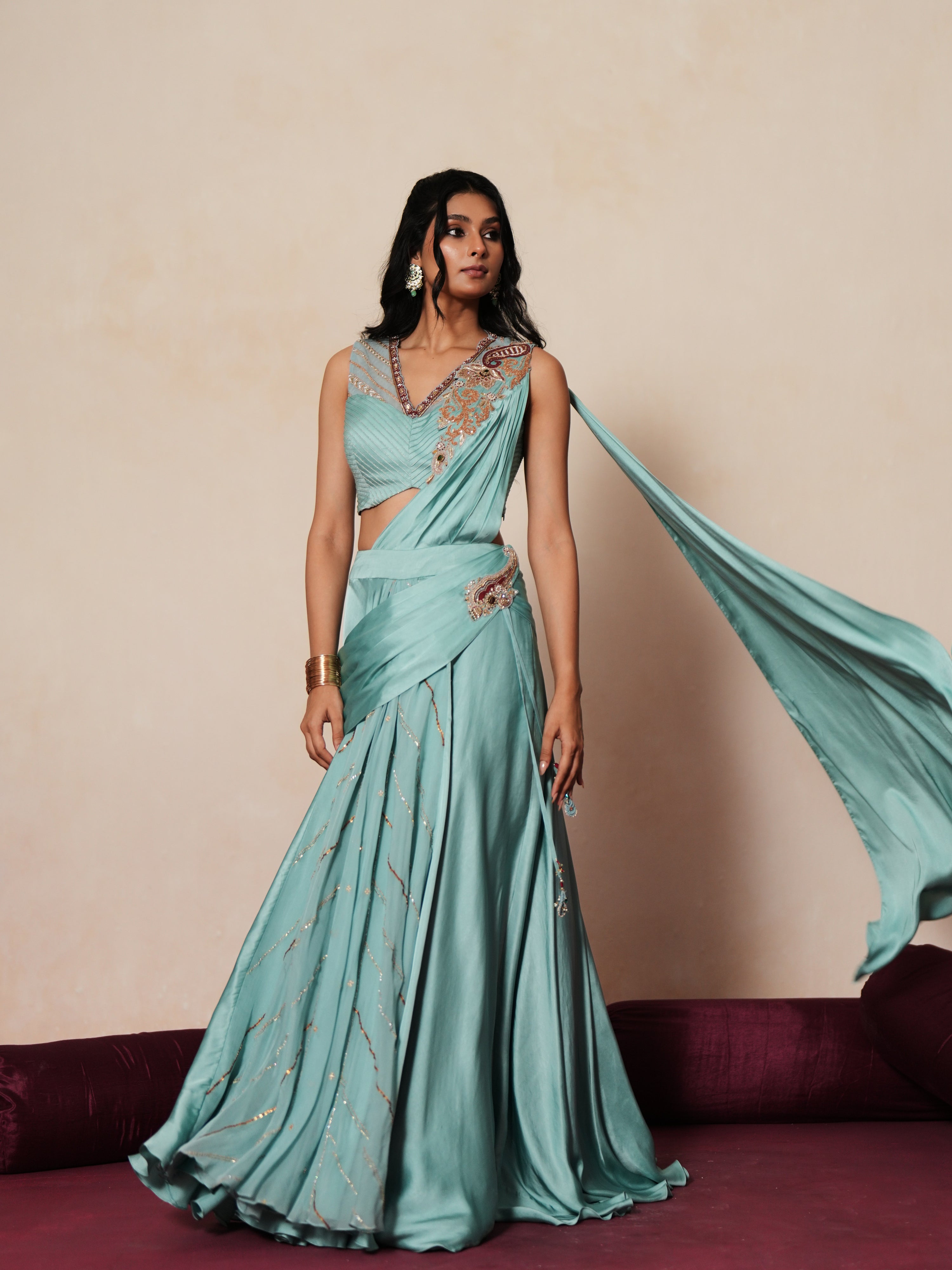 Woman in a pastel blue traditional outfit standing againsta beige wall on a red carpet.