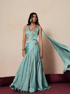 Woman in a pastel blue traditional outfit standing againsta beige wall on a red carpet.