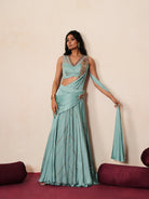 Woman in a pastel blue traditional outfit standing againsta beige wall on a red carpet.