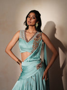 Woman in a pastel blue traditional outfit standing againsta beige wall on a red carpet.