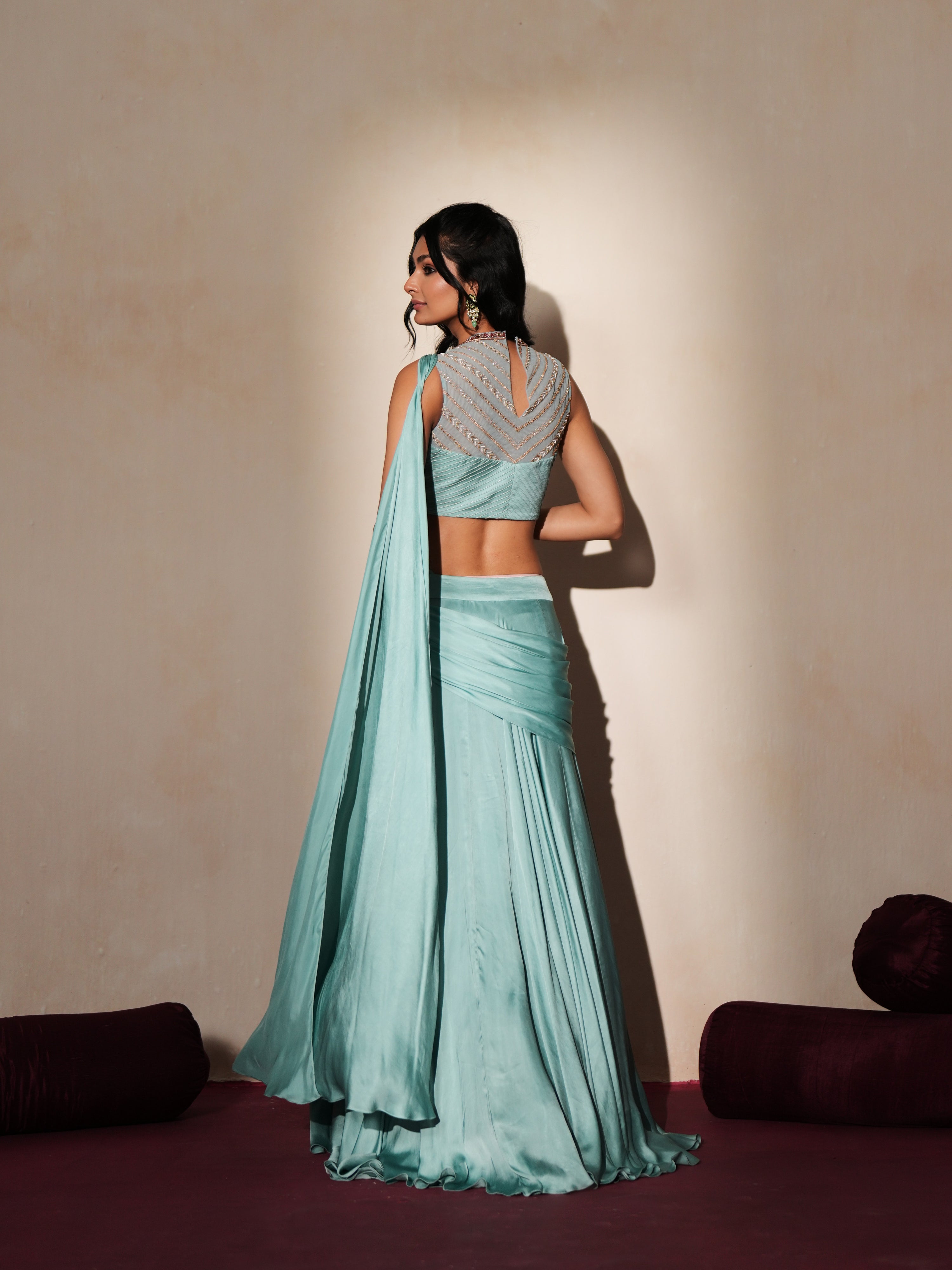 Woman in a pastel blue traditional outfit standing againsta beige wall on a red carpet.