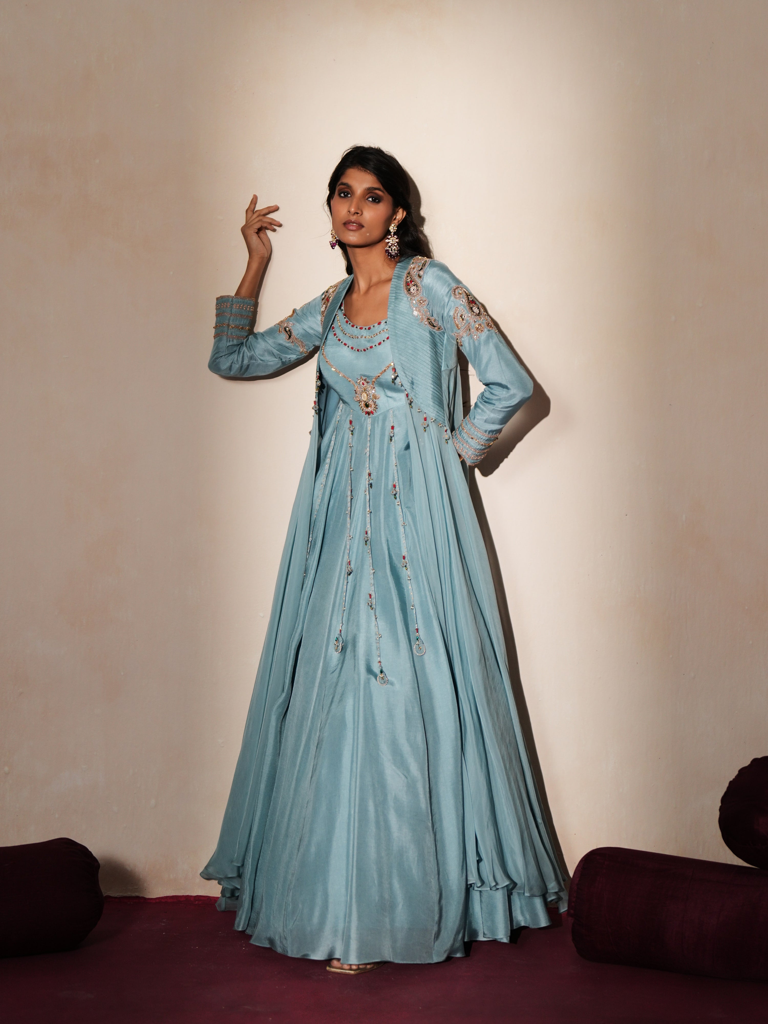 Woman in a pastel blue traditional outfit standing againsta beige wall on a red carpet.