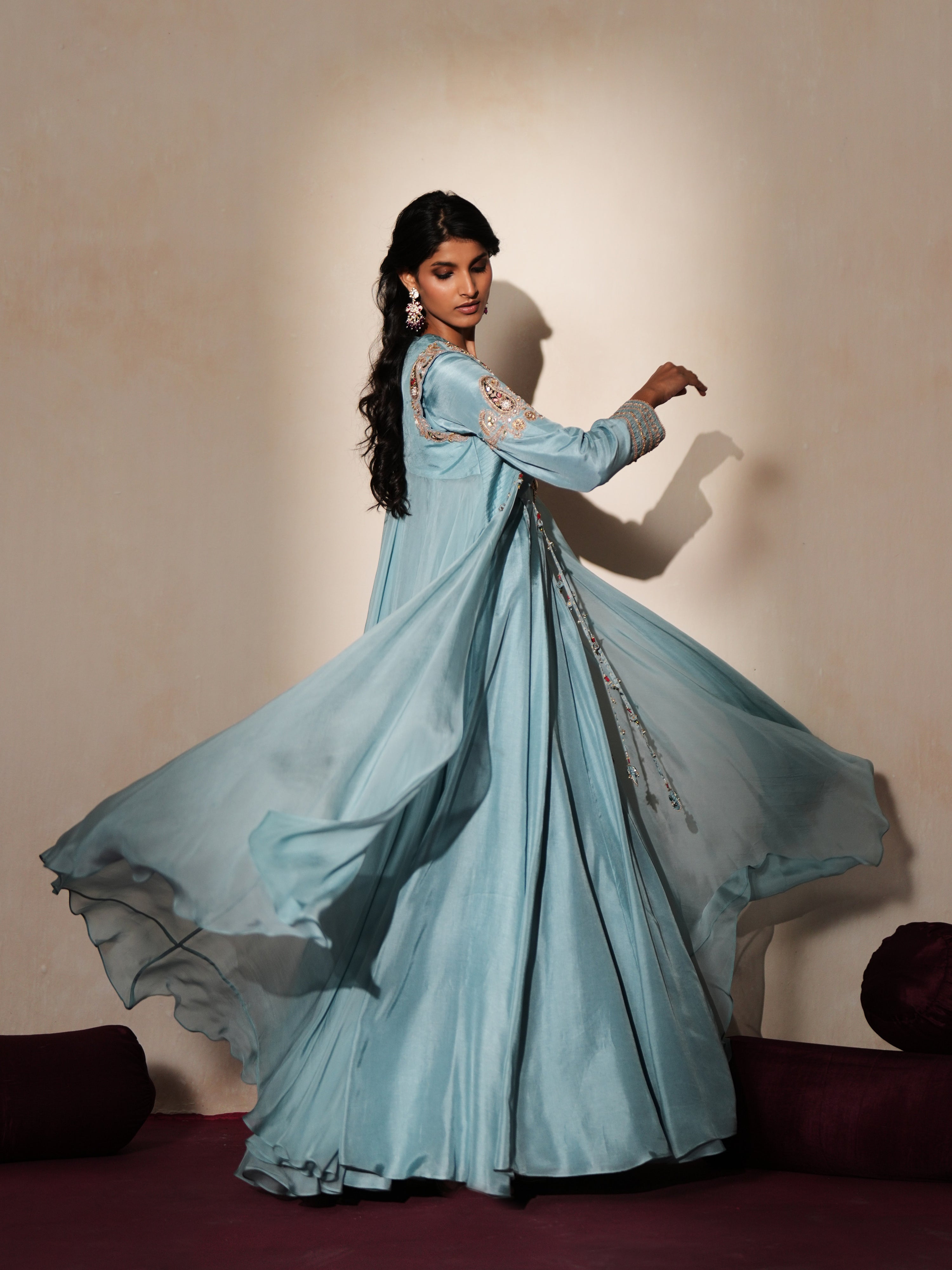 Woman in a pastel blue traditional outfit standing againsta beige wall on a red carpet.