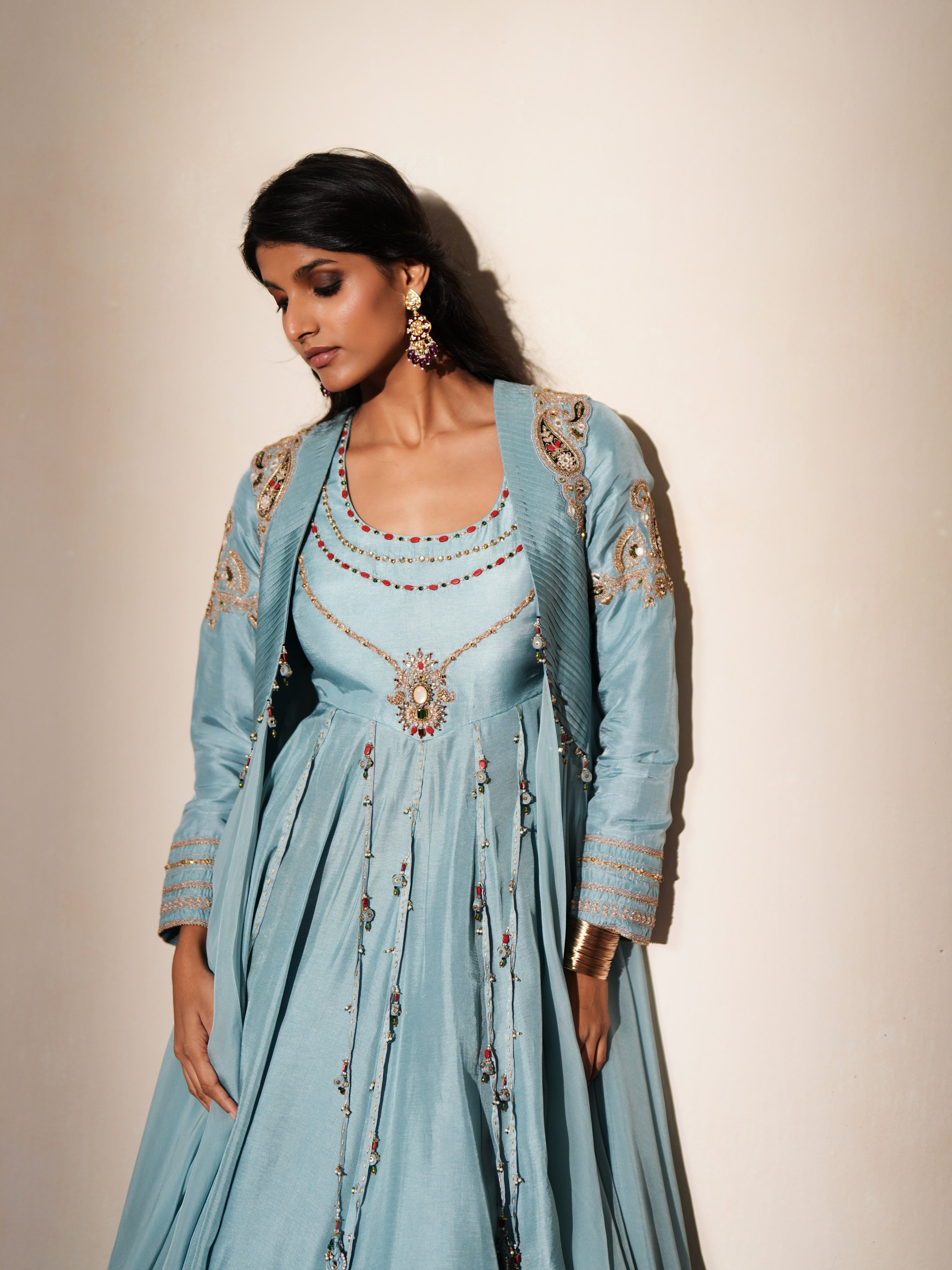 Woman in a pastel blue traditional outfit standing againsta beige wall on a red carpet.
