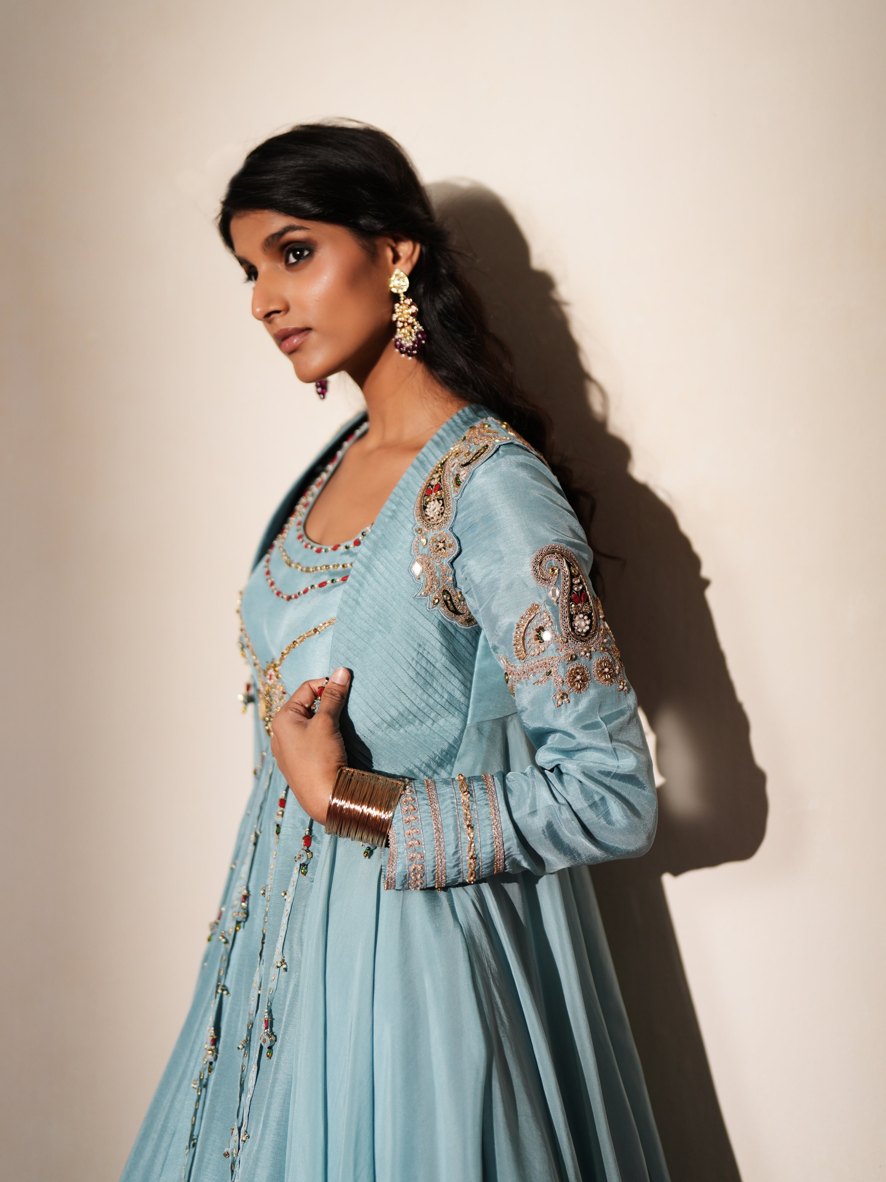 Woman in a pastel blue traditional outfit standing againsta beige wall on a red carpet.
