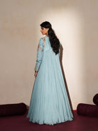 Woman in a pastel blue traditional outfit standing againsta beige wall on a red carpet.