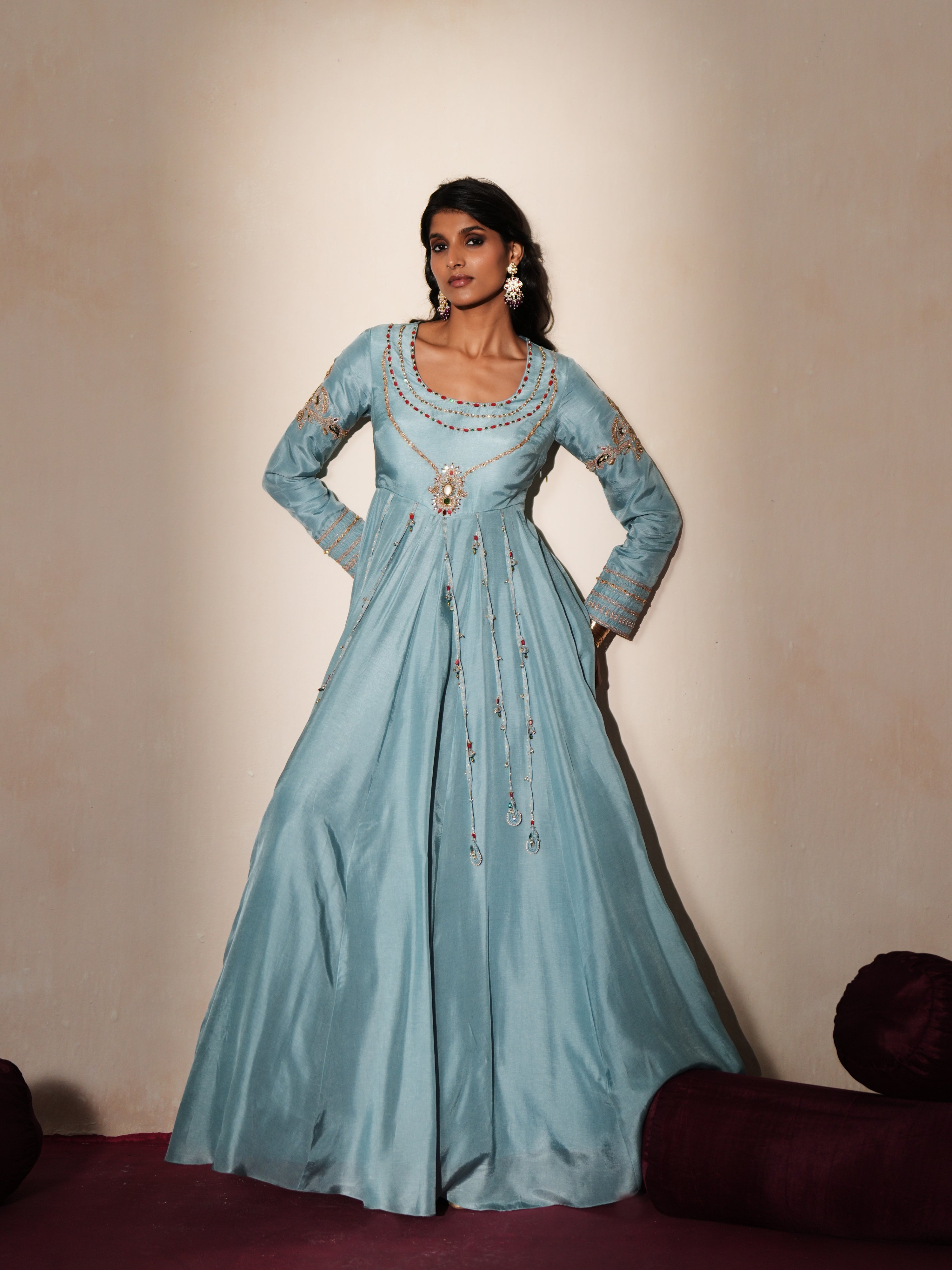 Woman in a pastel blue traditional outfit standing againsta beige wall on a red carpet.