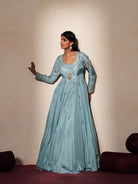 Woman in a pastel blue traditional outfit standing againsta beige wall on a red carpet.