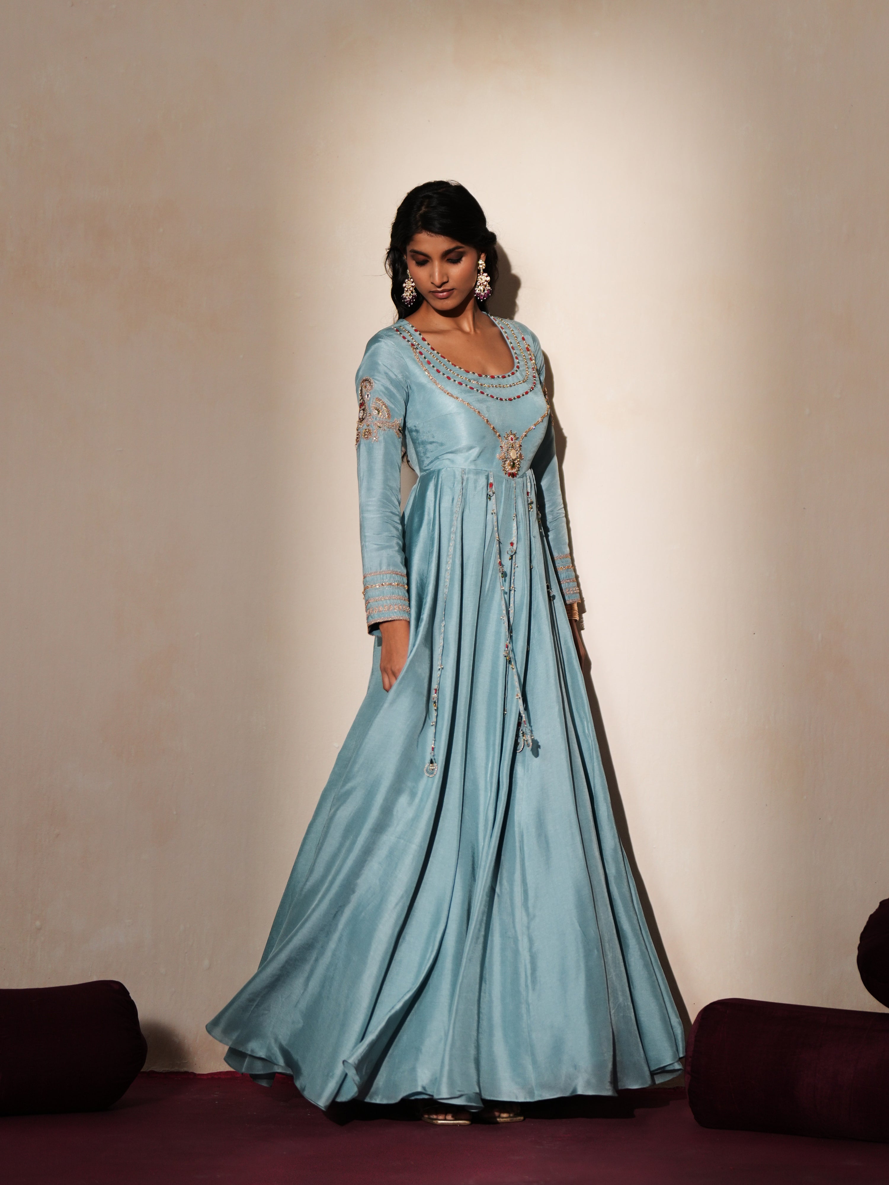 Woman in a pastel blue traditional outfit standing againsta beige wall on a red carpet.