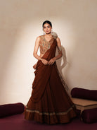 Woman in a mettalic brown traditional outfit standing againsta beige wall on a red carpet.