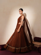 Woman in a mettalic brown traditional outfit standing againsta beige wall on a red carpet.