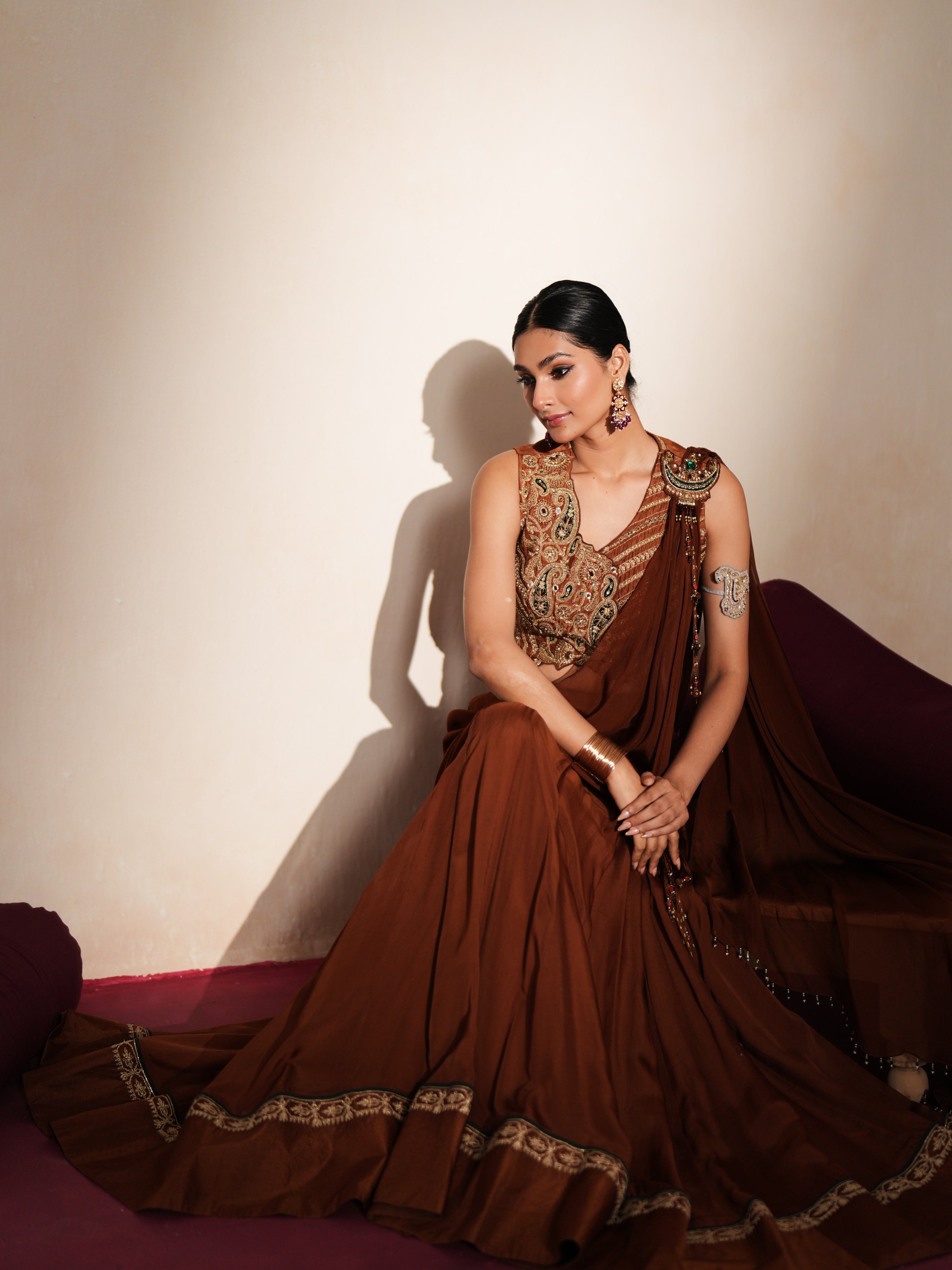 Woman in a mettalic brown traditional outfit standing againsta beige wall on a red carpet.