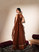 Woman in a mettalic brown traditional outfit standing againsta beige wall on a red carpet.