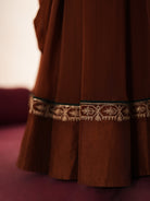 Woman in a mettalic brown traditional outfit standing againsta beige wall on a red carpet.