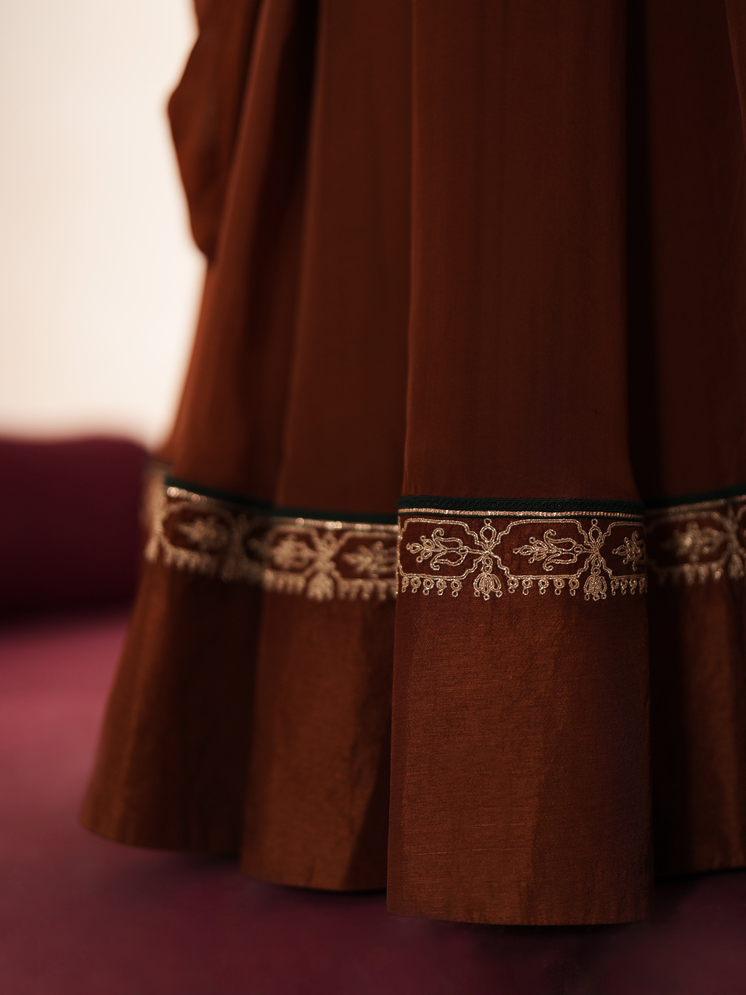 Woman in a mettalic brown traditional outfit standing againsta beige wall on a red carpet.