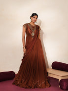 Woman in a mettalic brown traditional outfit standing againsta beige wall on a red carpet.