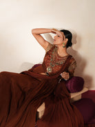 Woman in a mettalic brown traditional outfit standing againsta beige wall on a red carpet.
