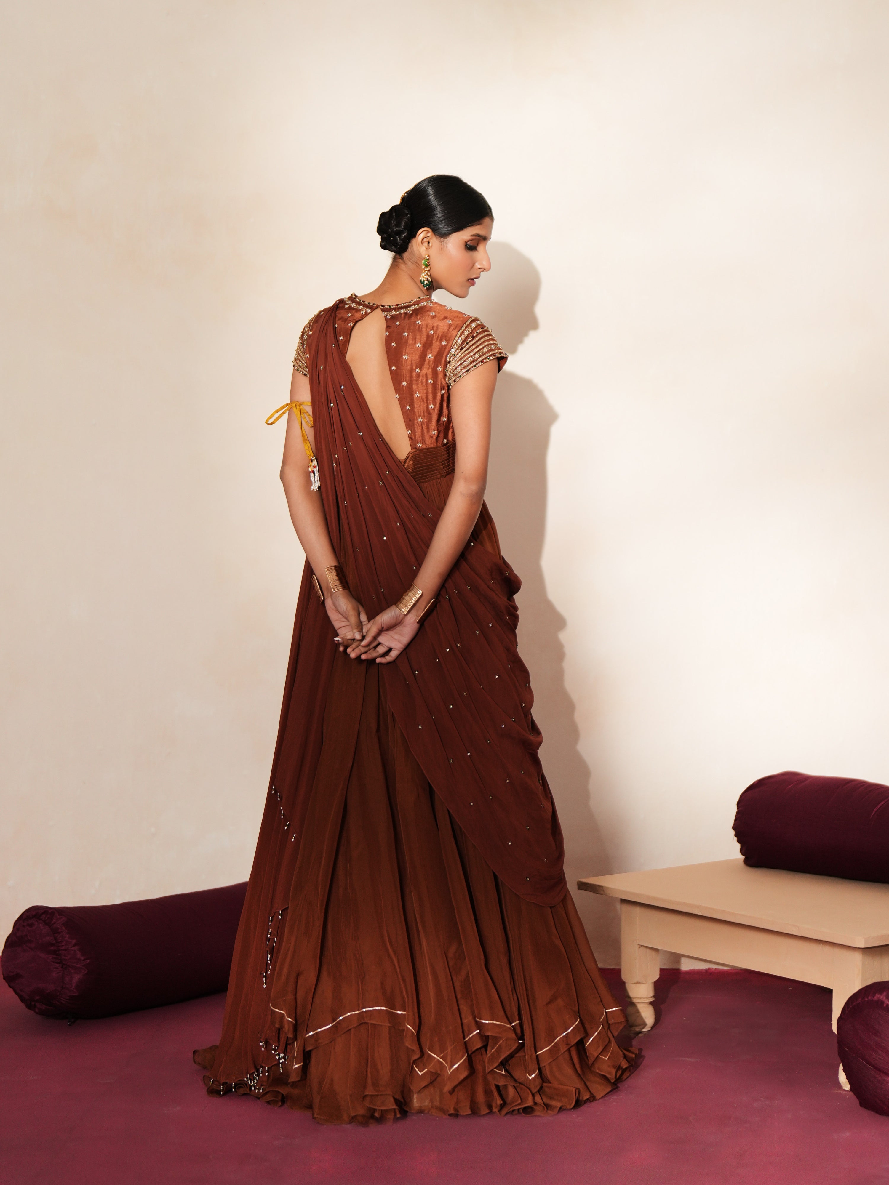 Woman in a mettalic brown traditional outfit standing againsta beige wall on a red carpet.