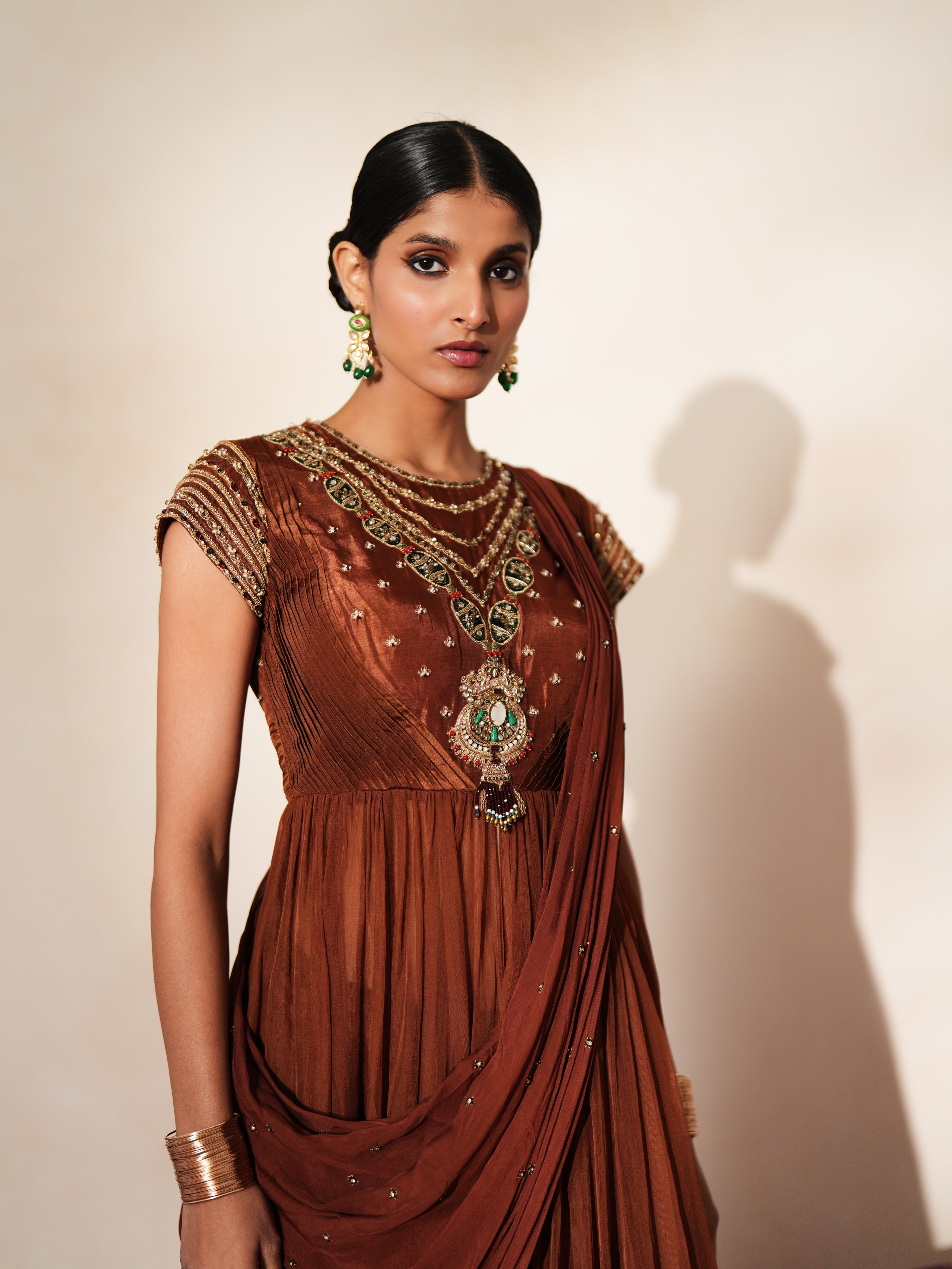 Woman in a mettalic brown traditional outfit standing againsta beige wall on a red carpet.