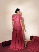 Woman in a mauve pink traditional outfit standing againsta beige wall on a red carpet.