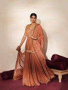 Woman in a metallic mocha  traditional outfit standing againsta beige wall on a red carpet.