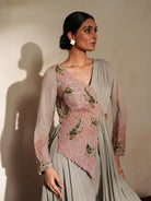 Woman in a mettalic grey traditional outfit standing againsta beige wall on a red carpet.