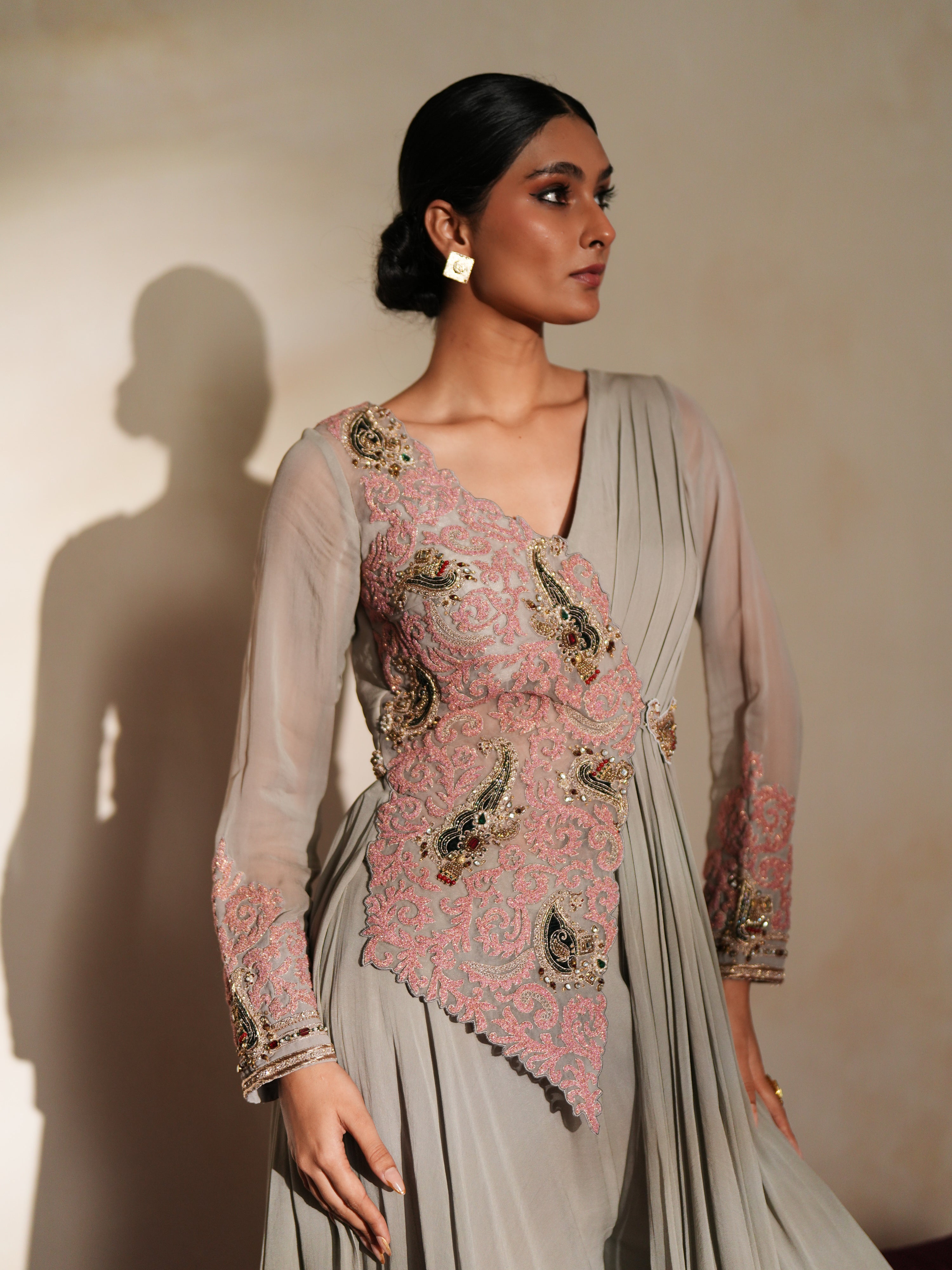 Woman in a mettalic grey traditional outfit standing againsta beige wall on a red carpet.