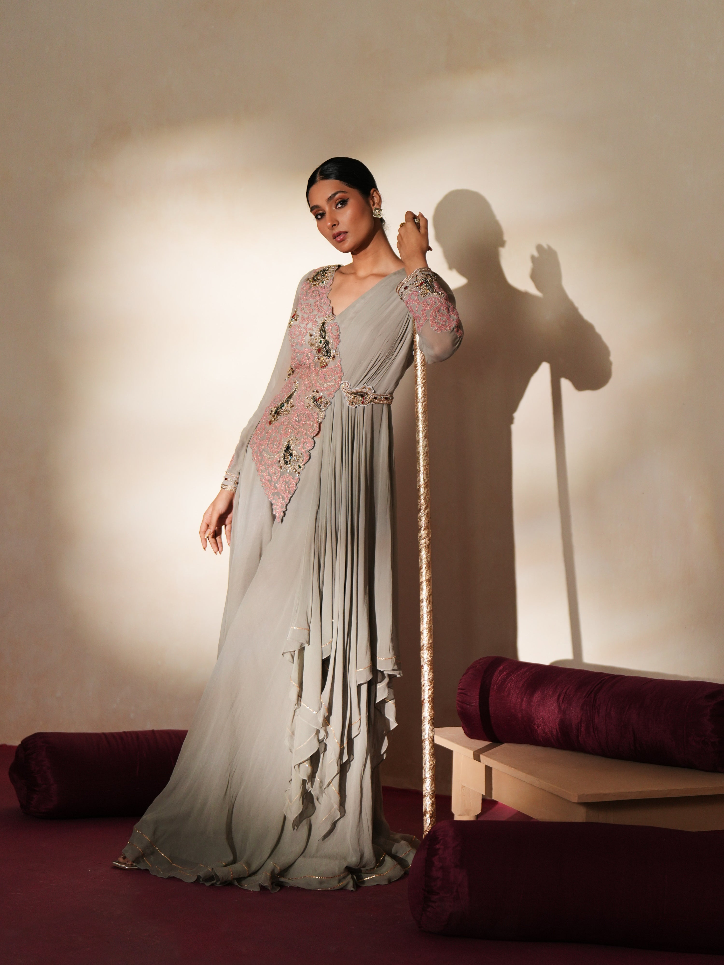 Woman in a mettalic grey traditional outfit standing againsta beige wall on a red carpet.