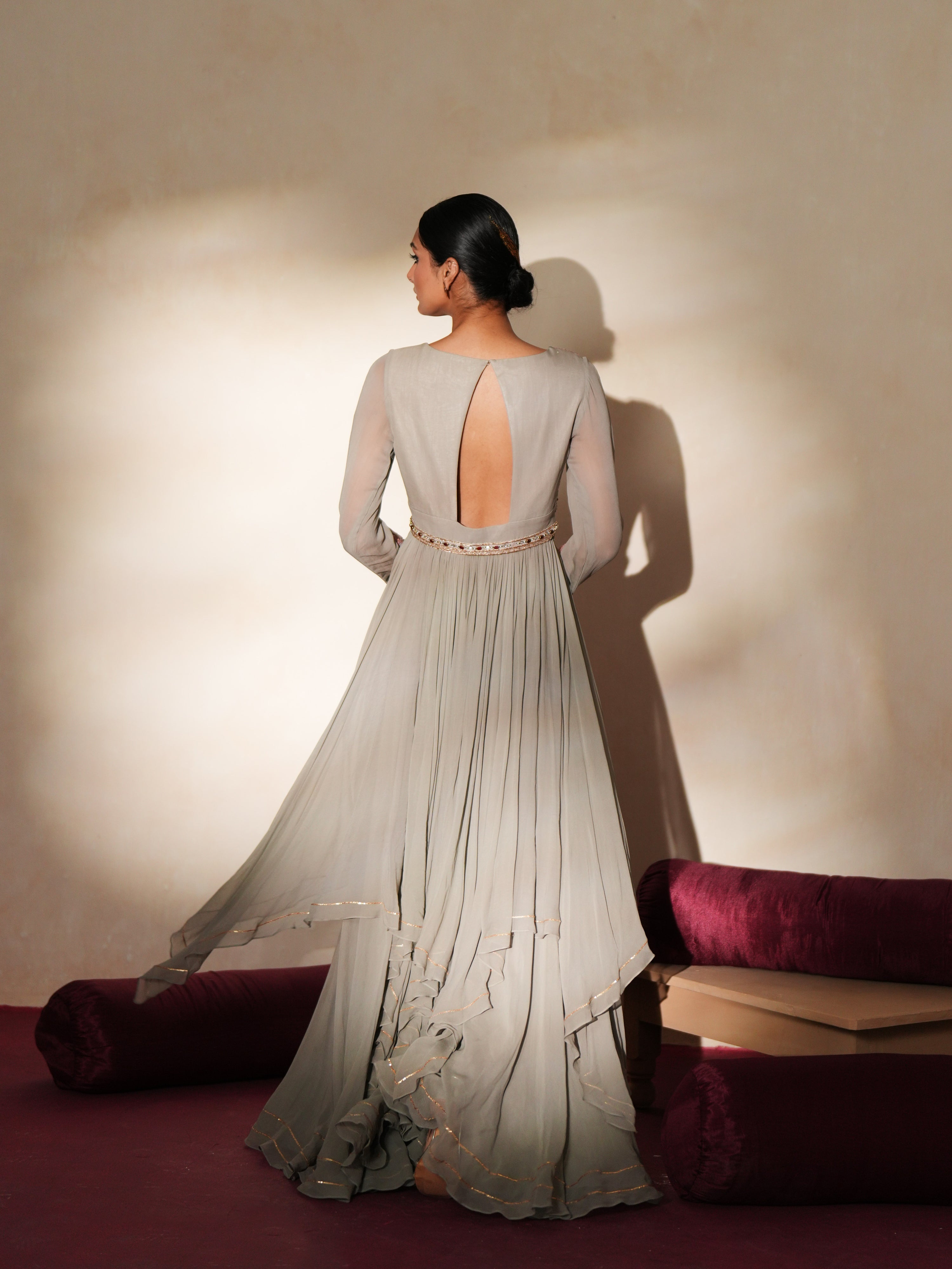 Woman in a mettalic grey traditional outfit standing againsta beige wall on a red carpet.