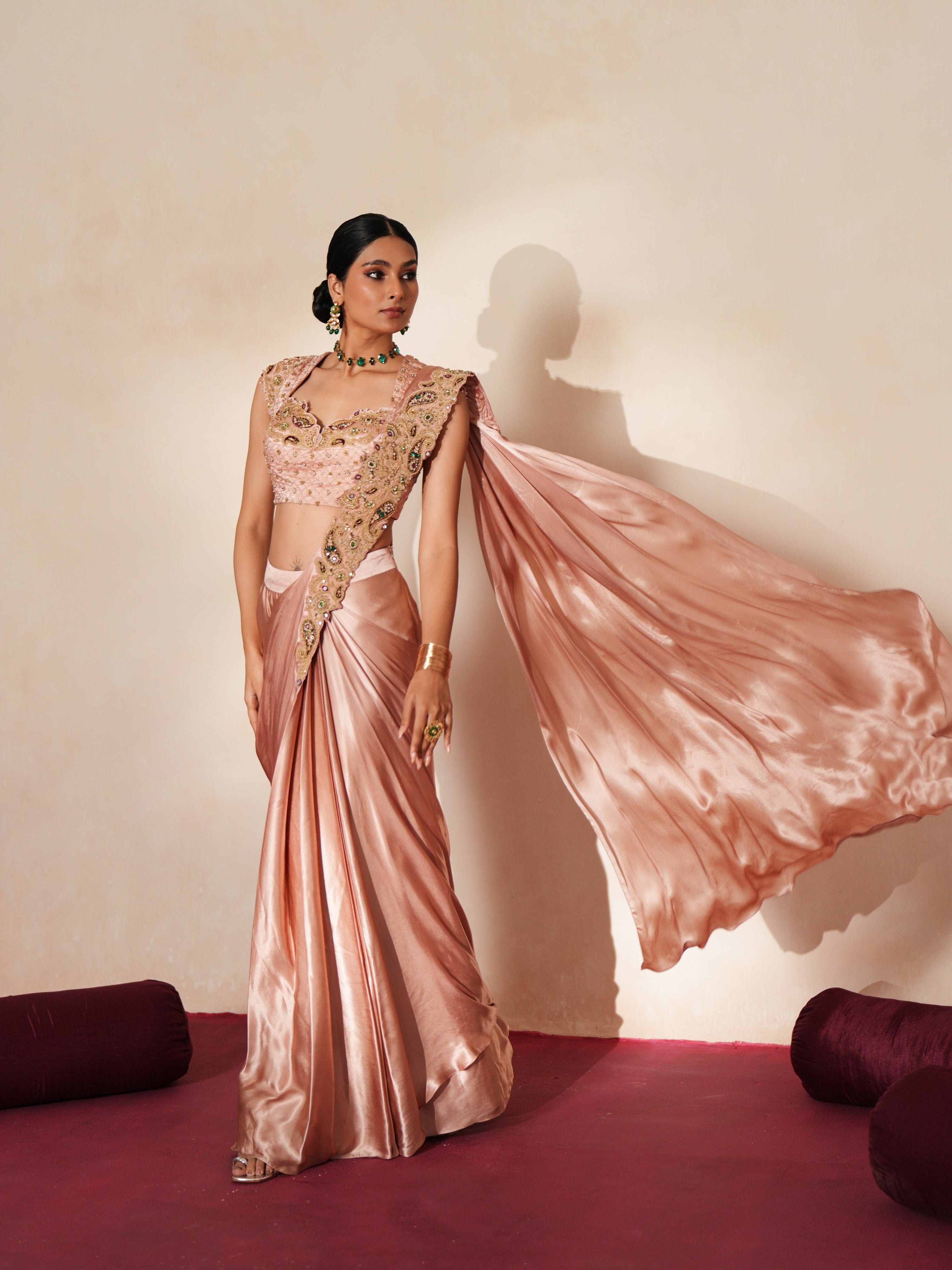 Woman in a soft pink traditional outfit standing againsta beige wall on a red carpet.