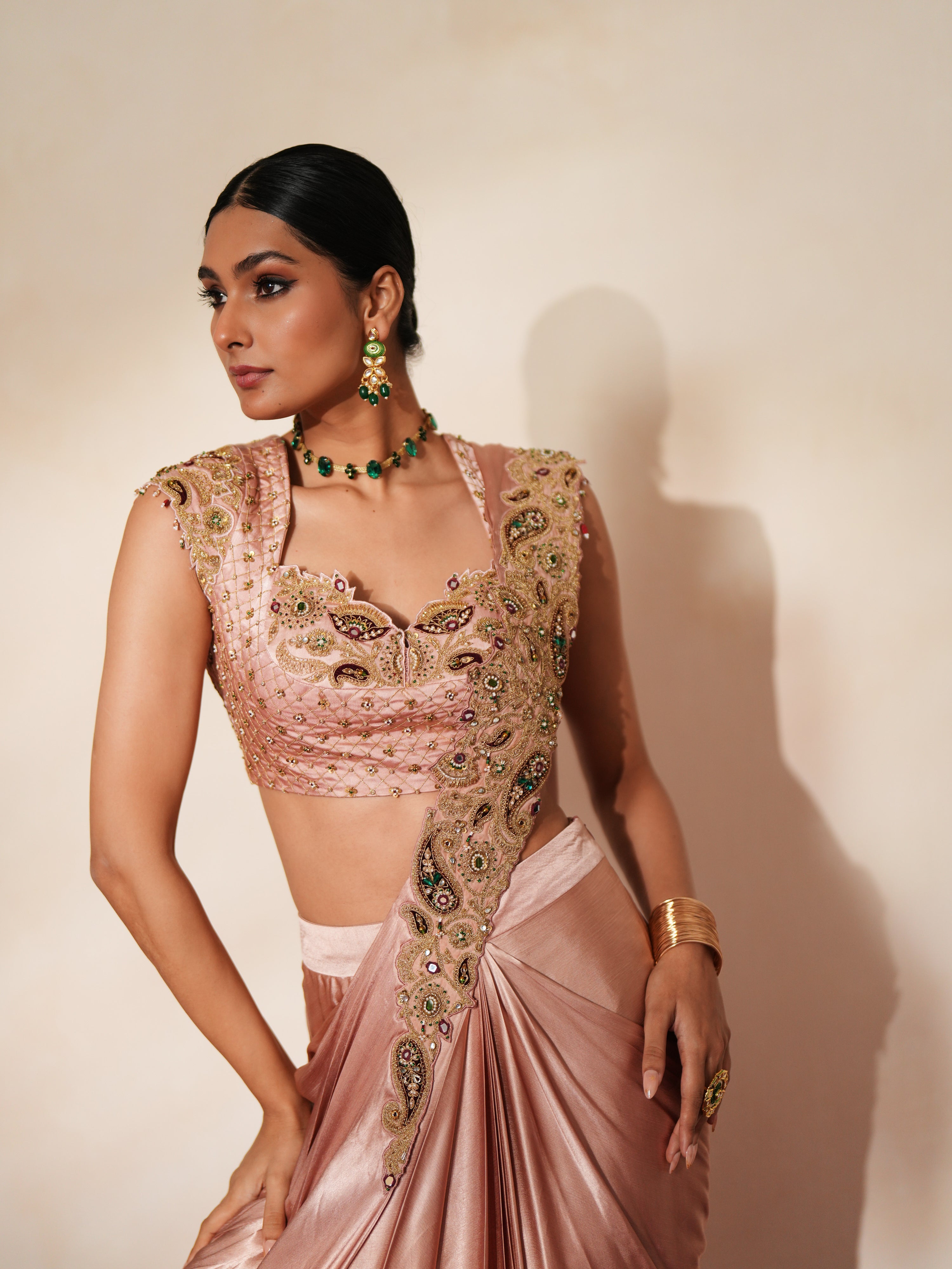 Woman in a soft pink traditional outfit standing againsta beige wall on a red carpet.