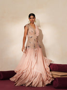 Woman in a soft pink traditional outfit standing againsta beige wall on a red carpet.