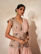 Woman in a soft pink traditional outfit standing againsta beige wall on a red carpet.