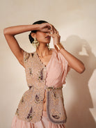 Woman in a soft pink traditional outfit standing againsta beige wall on a red carpet.