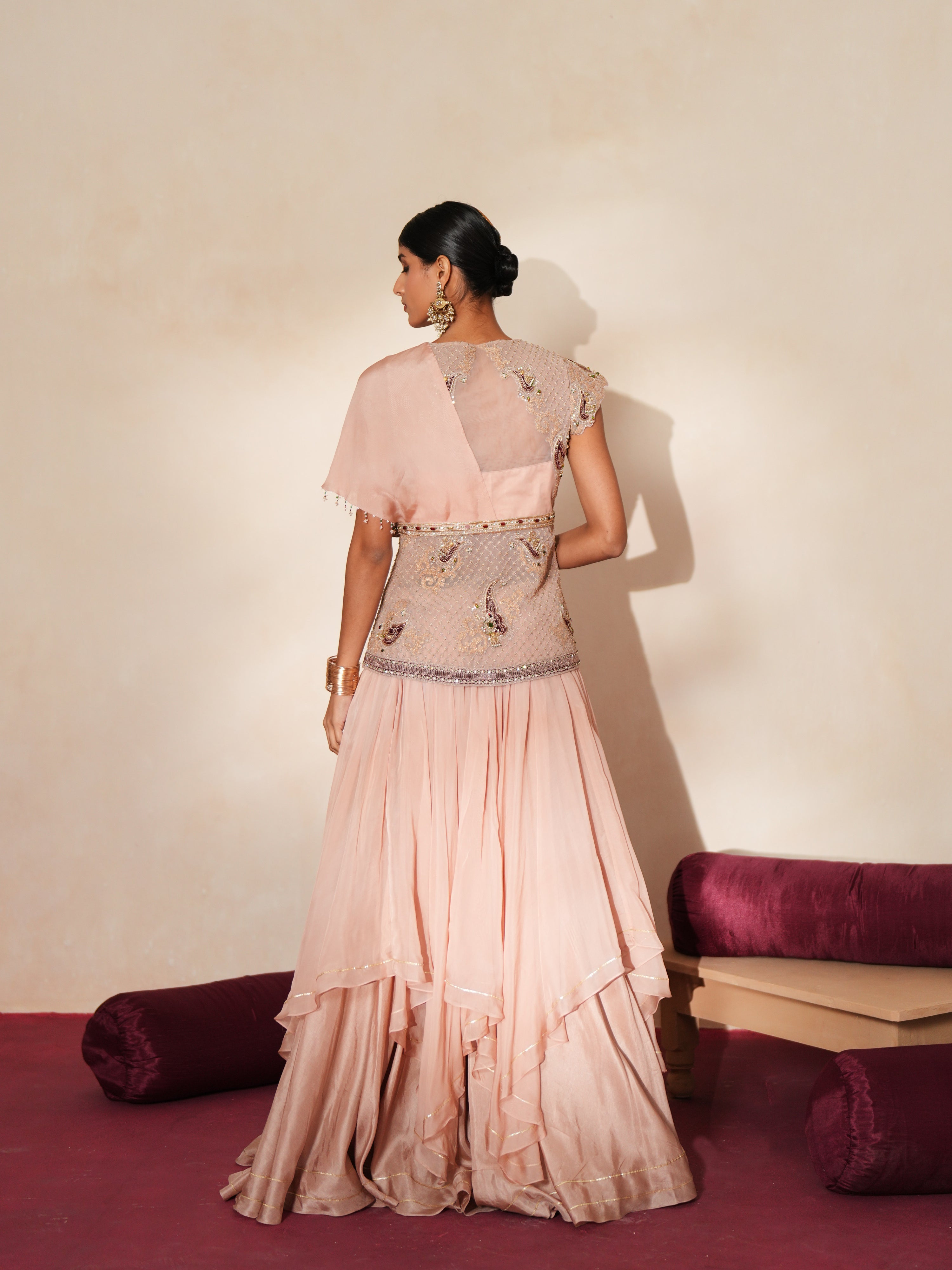 Woman in a soft pink traditional outfit standing againsta beige wall on a red carpet.