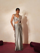 Woman in a mettalic grey traditional outfit standing againsta beige wall on a red carpet.