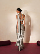 Woman in a mettalic grey traditional outfit standing againsta beige wall on a red carpet.