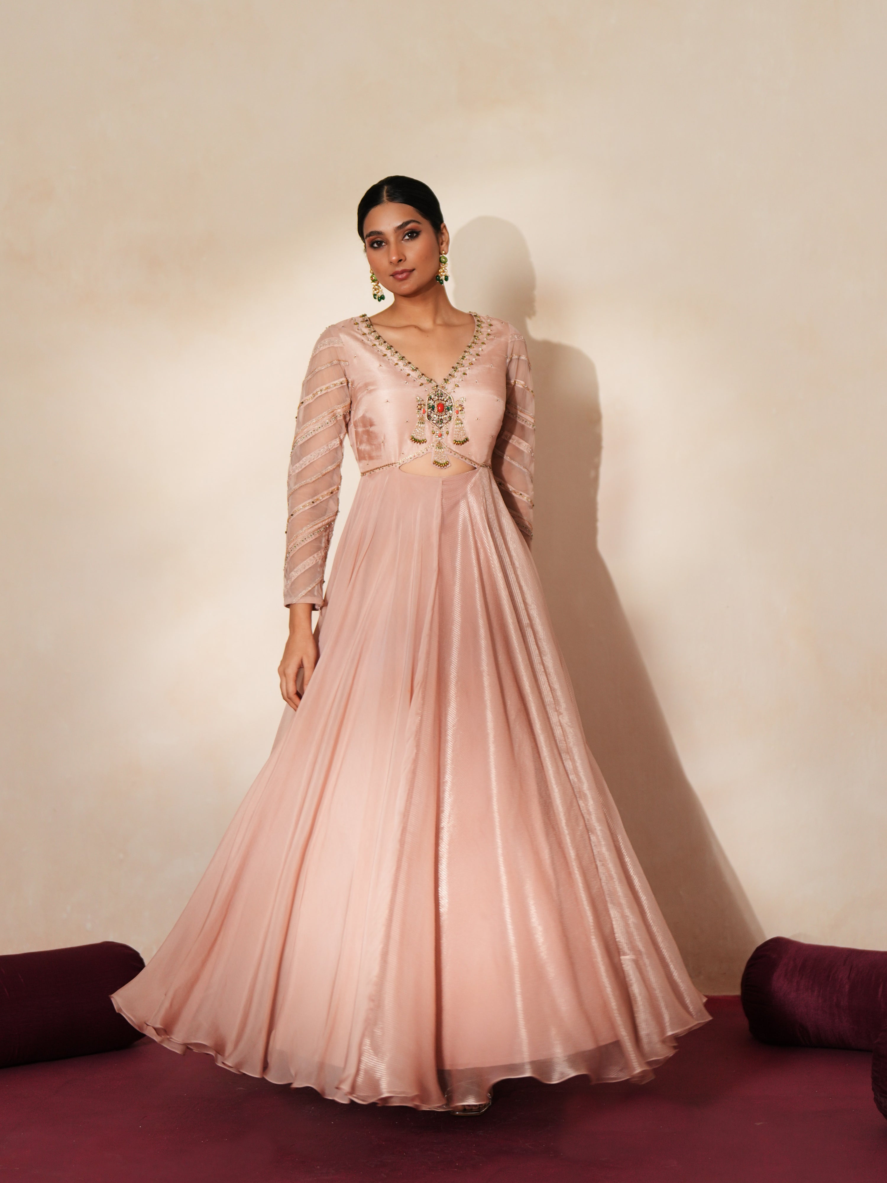 Woman in a soft pink traditional outfit standing againsta beige wall on a red carpet.